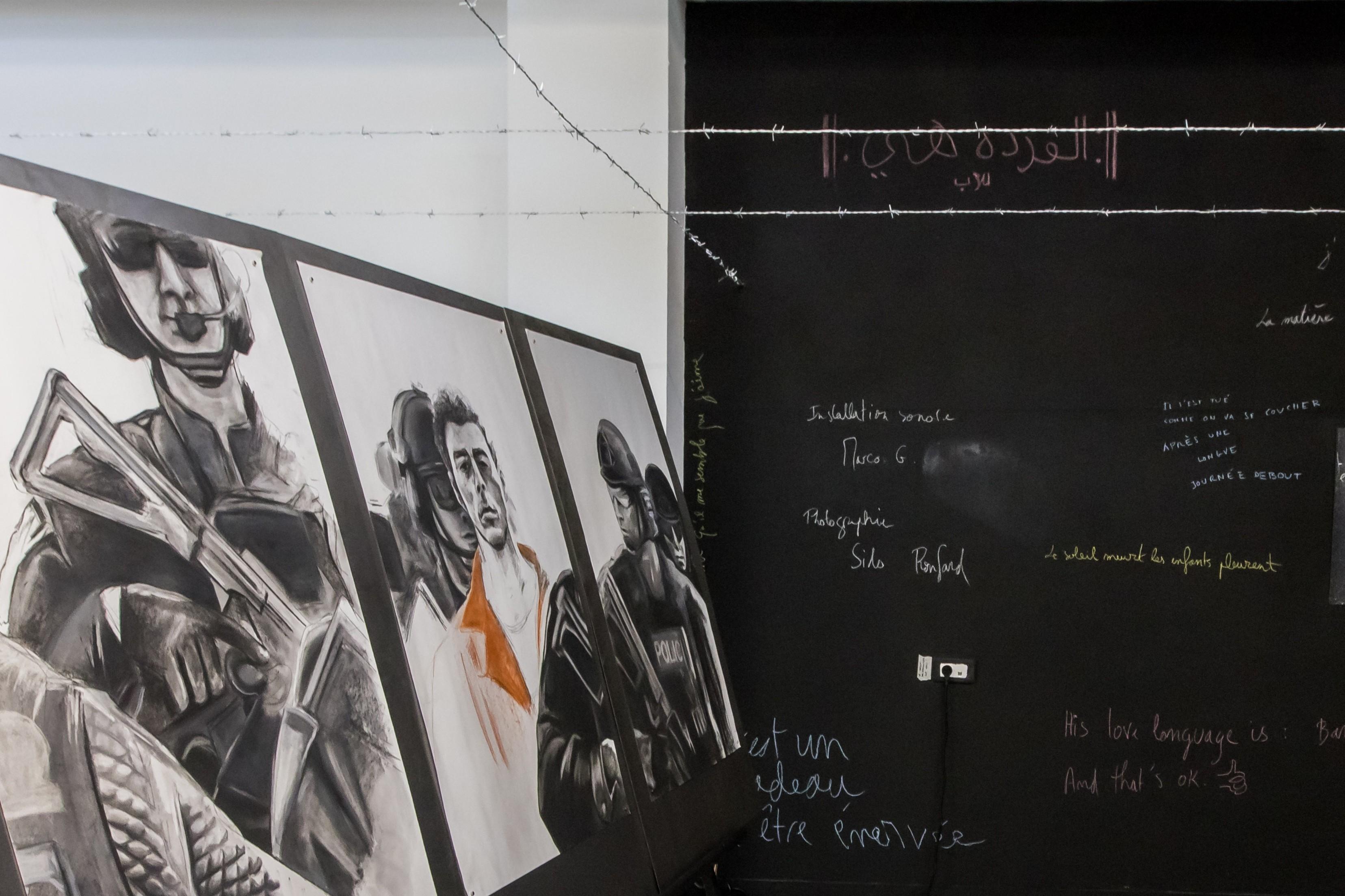 Trois dessins avec différentes personnes dessus. Au fond de la photo, un mur noir avec des écritures manuscrites. 